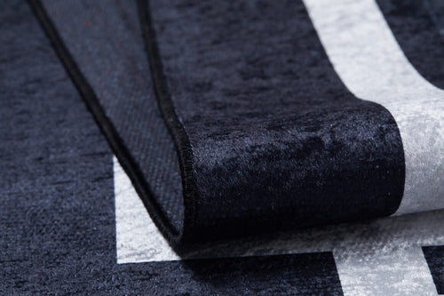 Load image 1 in gallery view. Close-up of the Subtle Border - Washable Rug - JR597 (Custom Size) in black with a white geometric pattern; one corner is folded to show its thick, textured build, making it durable and ideal for high-traffic areas.