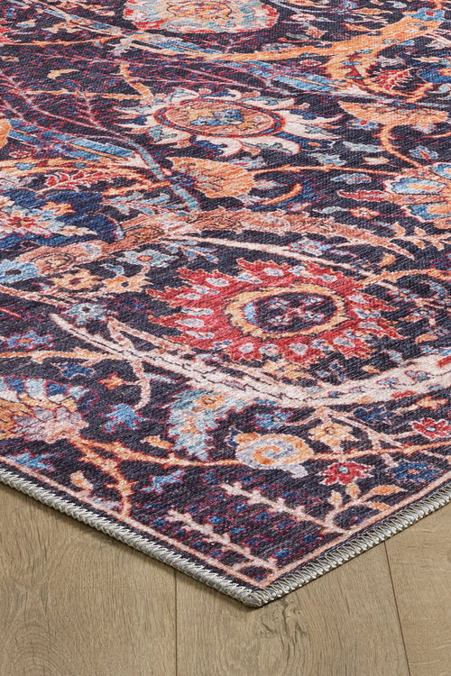Load image 1 in gallery view. A close-up of the Sylvanor Colorful Washable Rug - LCC3017 on a light wood floor, showing its intricate red, orange, blue, and cream floral patterns, detailed border, and textured edges in a Persian-inspired design.