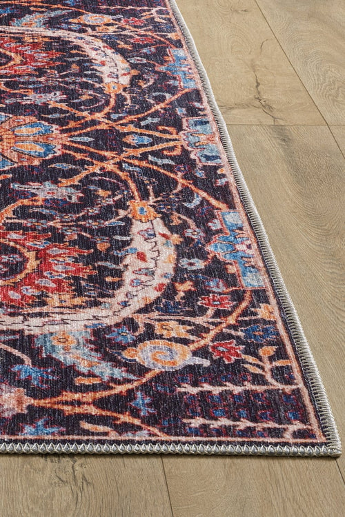 Load image 1 in gallery view. A close-up of the Sylvanor Colorful Washable Rug - LCC3017, showcasing its intricate red, blue, orange, and beige patterns on a light wood floor. This washable rug features detailed stitched edges and a vintage, slightly distressed look.