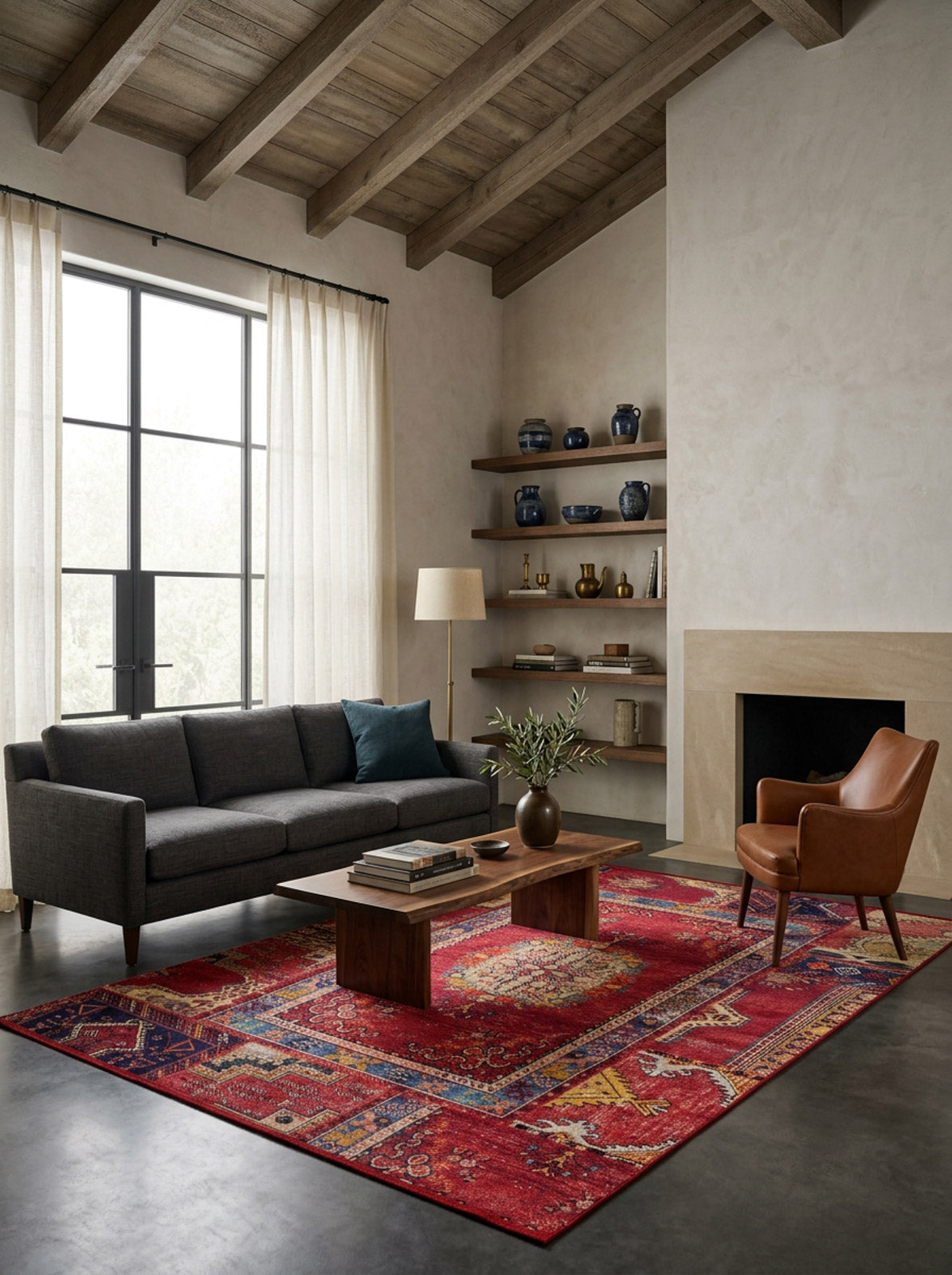 A modern living room with a gray sofa, brown leather chair, wooden coffee table, Tapestry Tango - Washable Rug - JR313 ideal for high-traffic areas, tall curtains, decorated shelves, floor lamp, and a fireplace beneath wood-beamed ceilings.