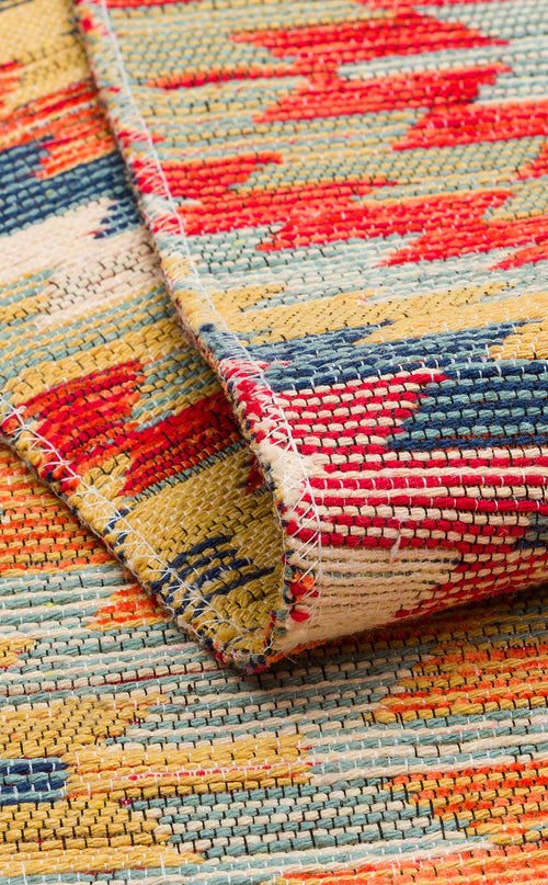 Load image 1 in gallery view. Close-up of the Terra Thread - Kilim - NMD07 rug featuring vibrant red, yellow, blue, and cream tribal patterns. A folded corner highlights its textured weave and detailed stitching along the edge.