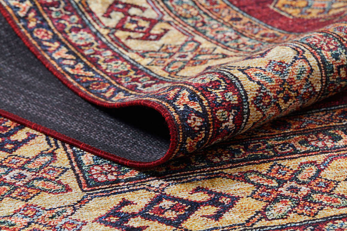 A close-up of the Time-Honored Textures - Washable Rug - JR40 (Custom Size) reveals red tones with geometric and floral designs in yellow, navy, and cream. Folded edge shows texture—perfect as a washable rug for high-traffic areas.
