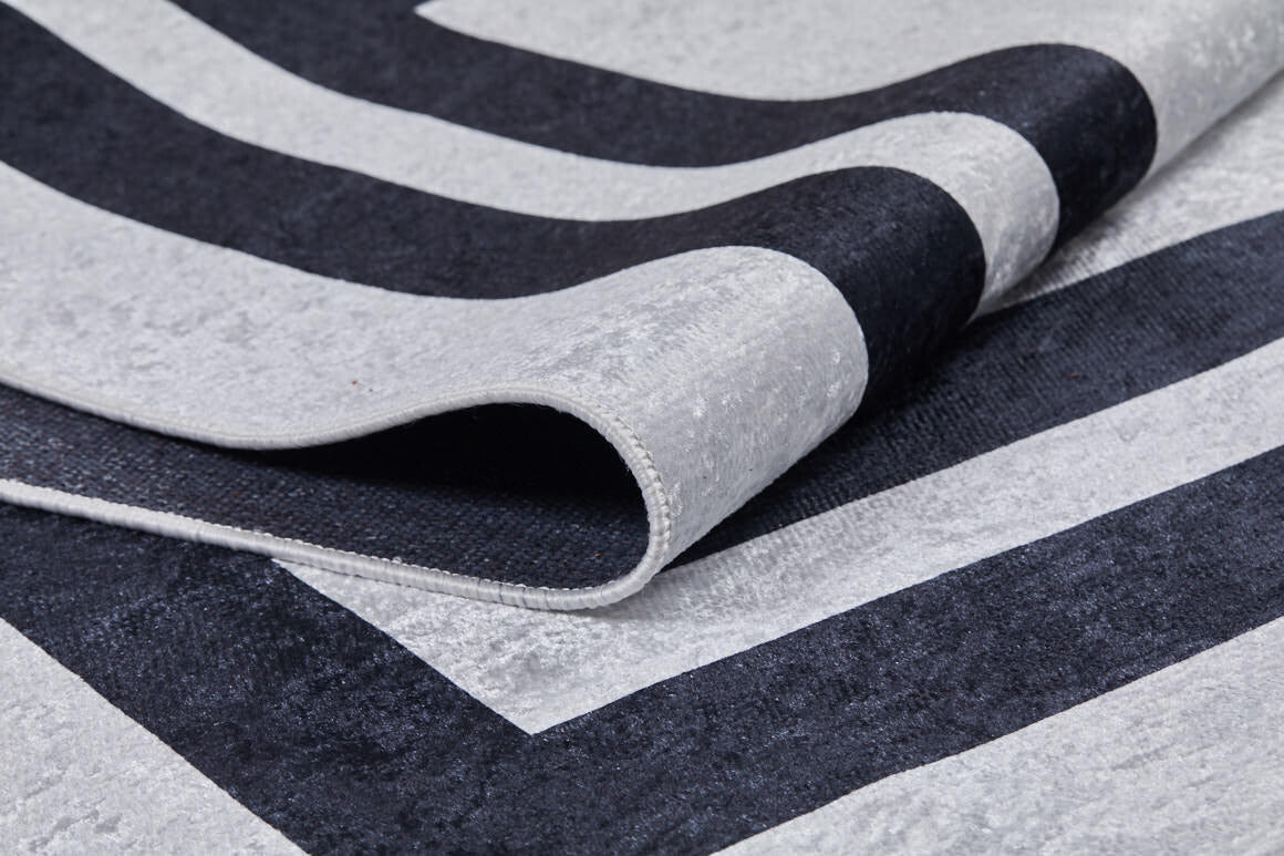 A close-up of the Timeless Border - Washable Rug - JR572 (Custom Size) shows its gray-anthracite tones with black and light gray geometric stripes. The fold reveals texture and thickness—ideal for high-traffic areas.