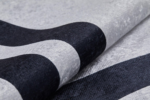 Load image 1 in gallery view. Close-up of the Timeless Border - Washable Rug - JR572 (Custom Size) in gray-anthracite with bold, curved black stripes. Its soft, subtly shiny material is partially folded—durable and washable for high-traffic areas.