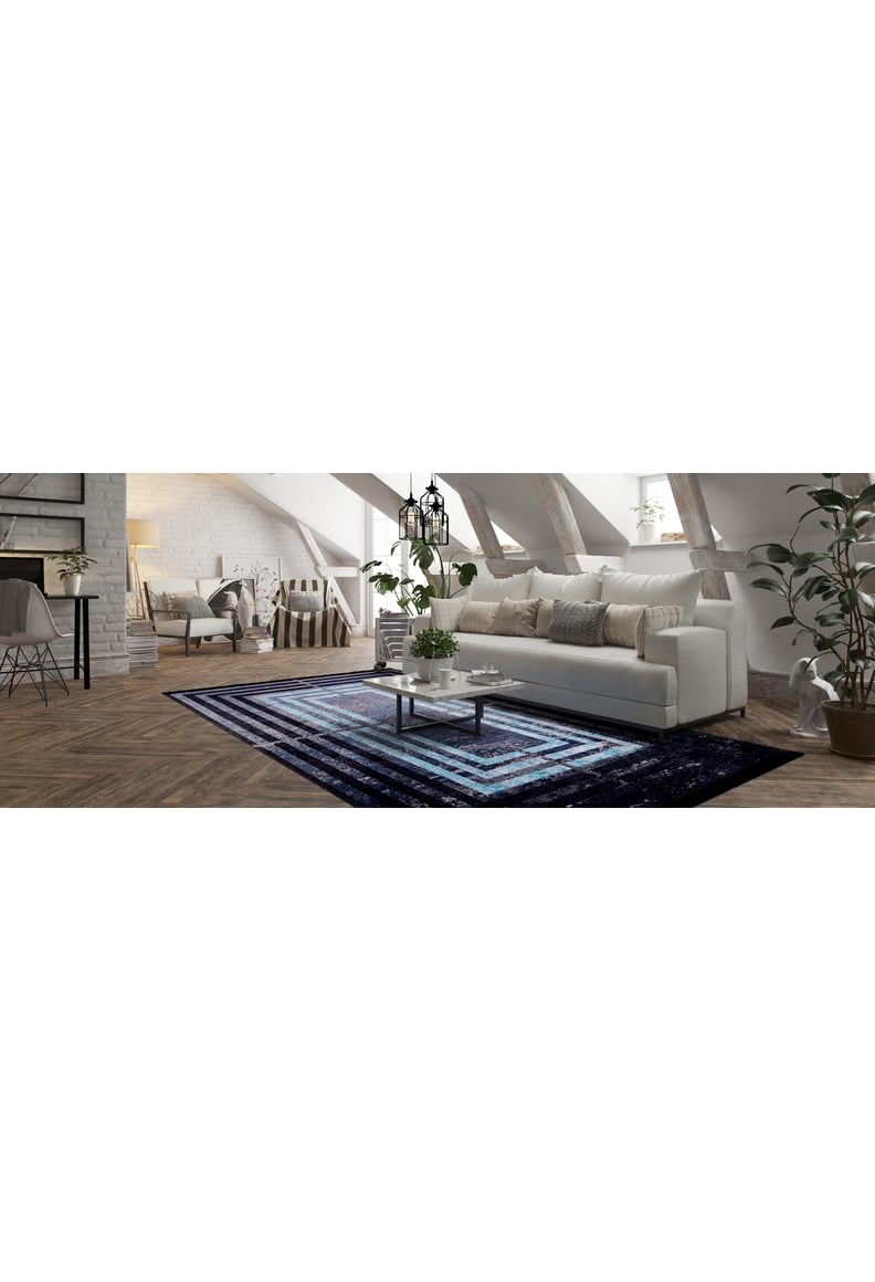 A bright attic living room with white walls, a white sofa, coffee table, plants, exposed wooden beams, and the Traditional and Timeless - Washable Rug - JR1408 in navy and blue for high-traffic areas. Natural light fills the space.