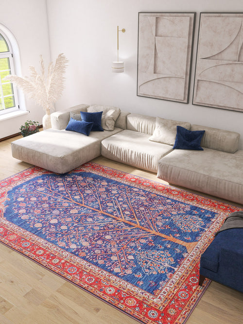 Load image 1 in gallery view. A bright living room features a beige sectional sofa, blue throw pillows, abstract wall art, and the Tree of Plenty Red Blue Washable Rug—ideal for allergy-sensitive households and high-traffic areas. Pampas grass decor stands by the window.