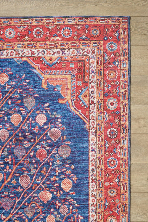 Load image 1 in gallery view. Tree of Plenty Red Blue Washable Rug (LCC3031) features a blue floral center, red, orange, and cream border motifs; it’s washable and ideal for allergy-sensitive homes or high-traffic areas. Shown on a light wood floor.