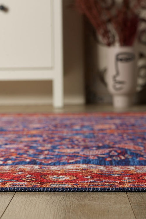 Load image 1 in gallery view. A close-up of the Tree of Plenty Red Blue Washable Rug (LCC3031) on a wooden floor, with a white cabinet and a face-design vase in the blurred background—ideal for high-traffic areas.