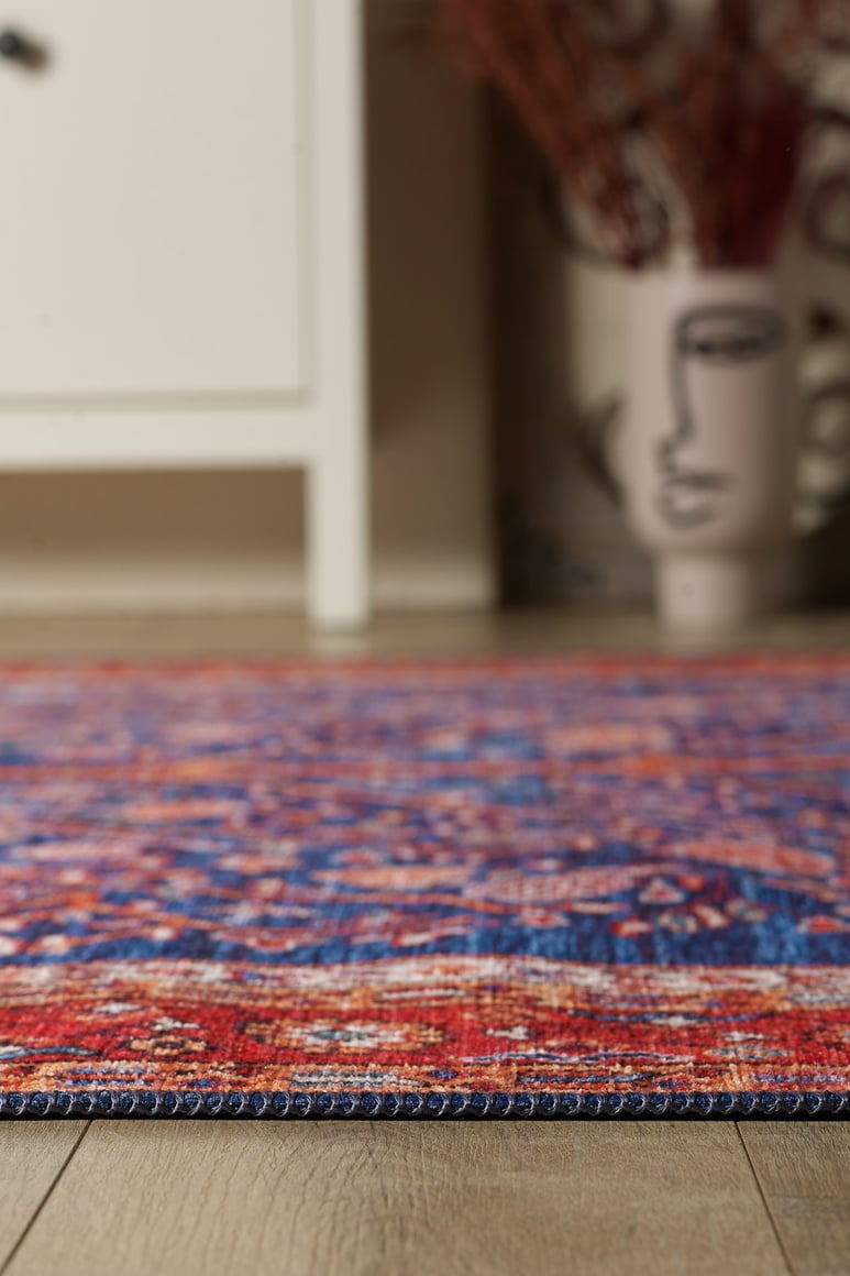 A close-up of the Tree of Plenty Red Blue Washable Rug - LCC3031 (Custom Size) on a wooden floor, with a white cabinet and an abstract face vase in the background—ideal for allergy-sensitive or high-traffic homes.