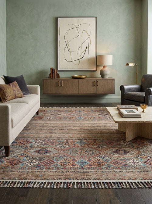 Load image 1 in gallery view. A modern living room featuring a beige sofa, dark armchair, stone coffee table, and the Tribal Tango - Washable Rug - JR5089—ideal for high-traffic areas—plus a floating wood console with decor, lamp, and abstract art on a green wall.