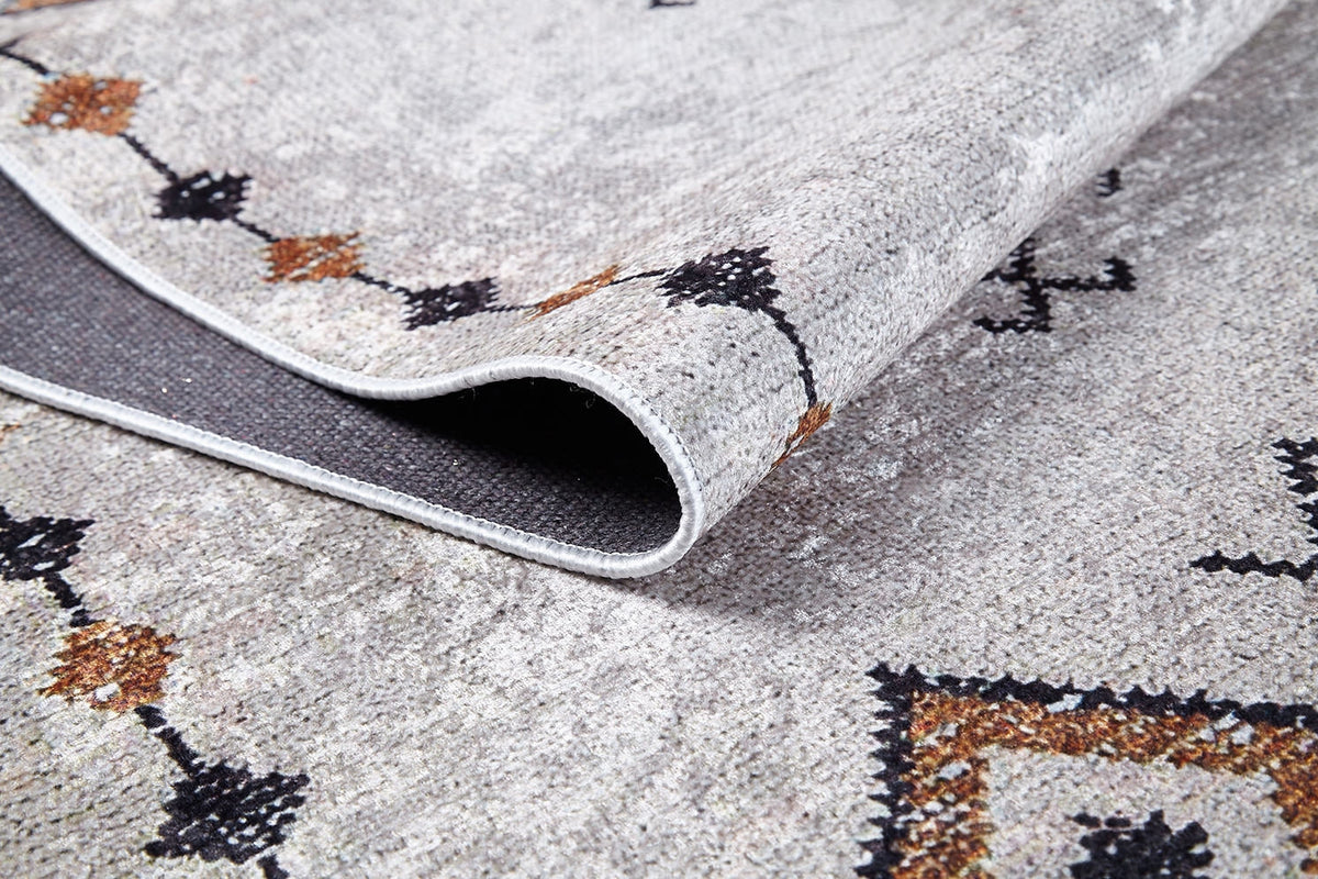 A close-up of the Tribal Tassel - Washable Rug - JR1683 (Custom Size) highlights its textured, patterned surface and underside. With a light gray base and black/brown geometric motifs, it’s ideal for allergy-sensitive homes seeking style and convenience.