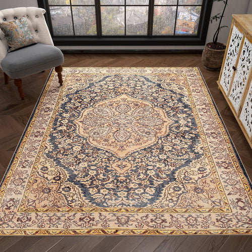 Load image 1 in gallery view. The Majestic Crest - Washable Rug - JRN1015, featuring intricate floral and medallion patterns in beige, cream, and navy blue, decorates a wooden floor in a cozy room with a cushioned chair, potted plant, and large windows.