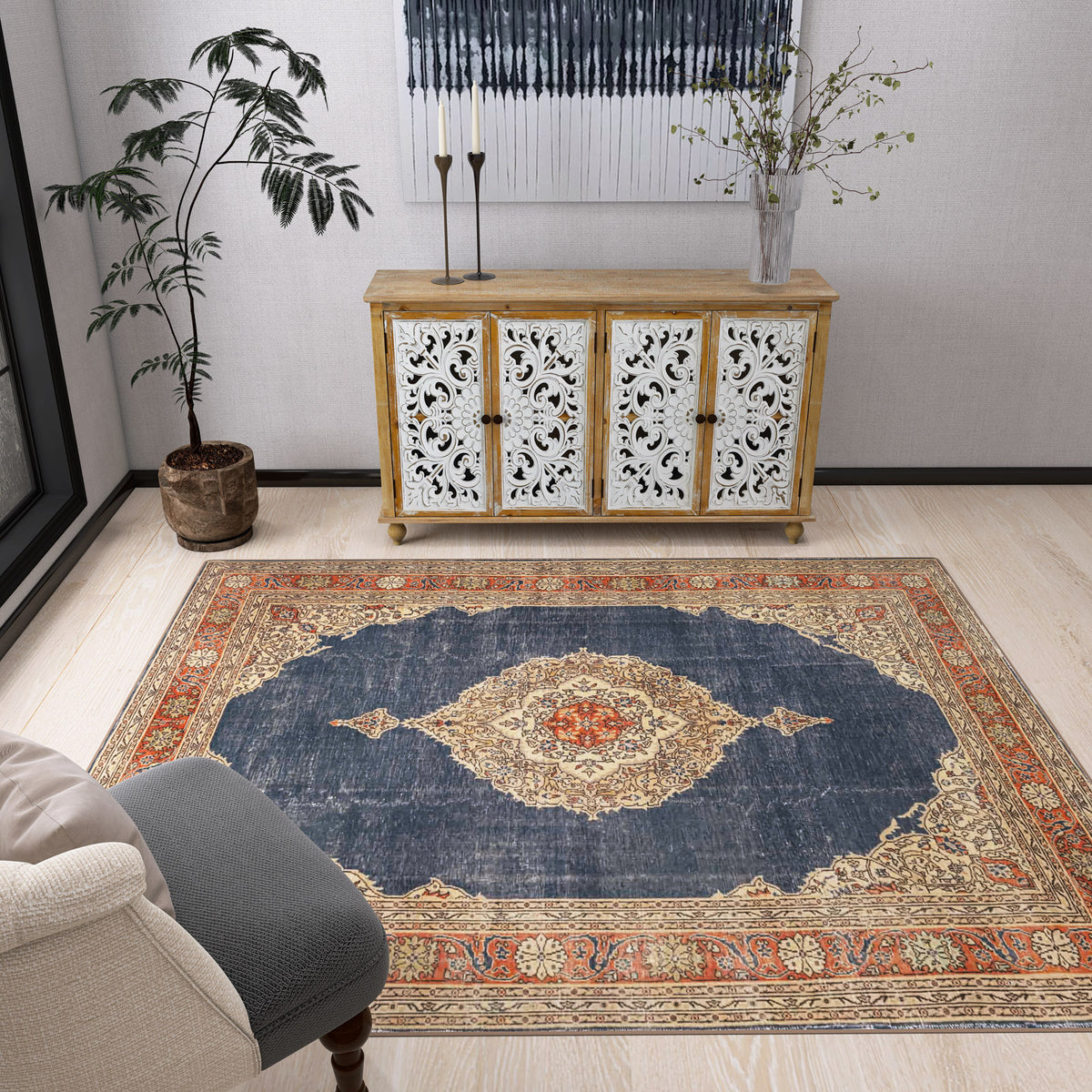 A cozy living room features the Antique Symphony - Washable Rug - JRN1017 with a medallion design, a cream armchair, potted plant, ornate white sideboard, and vase with branches—perfect for traditional interiors.