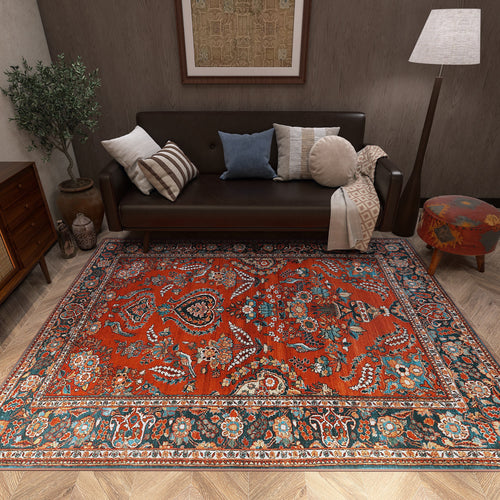 Load image 1 in gallery view. A cozy living room with a dark sofa, assorted pillows, potted plant, floor lamp, and the Golden Scrolls - Washable Rug - JRN1005 adding vibrant red, blue, and orange accents over a wooden herringbone floor.