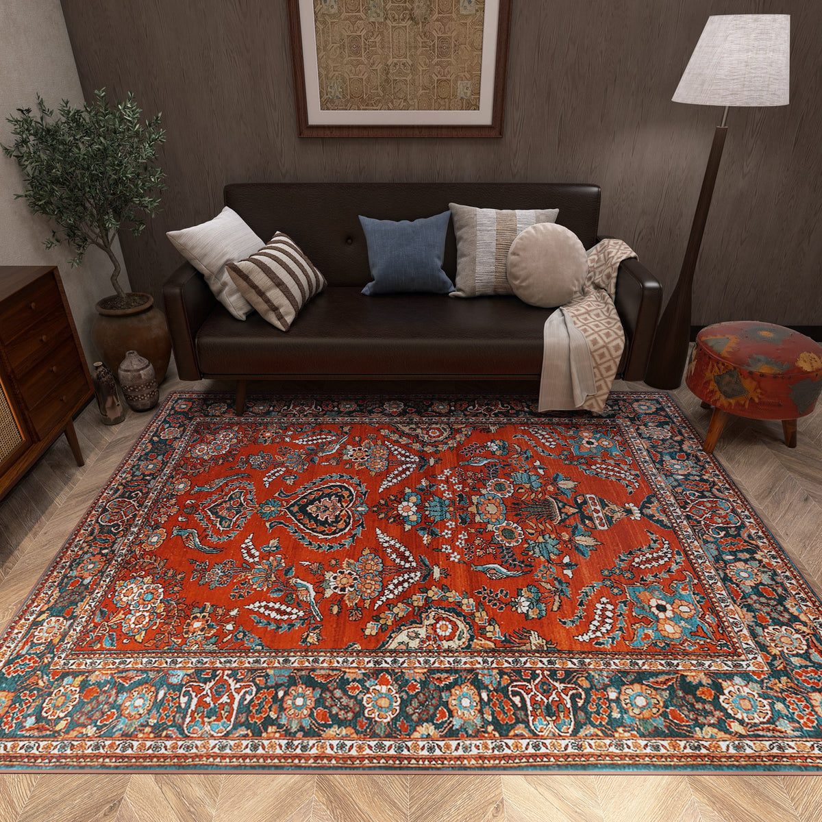 Rust-red traditional rug with intricate floral and medallion patterns, styled in a living room with a dark leather sofa.