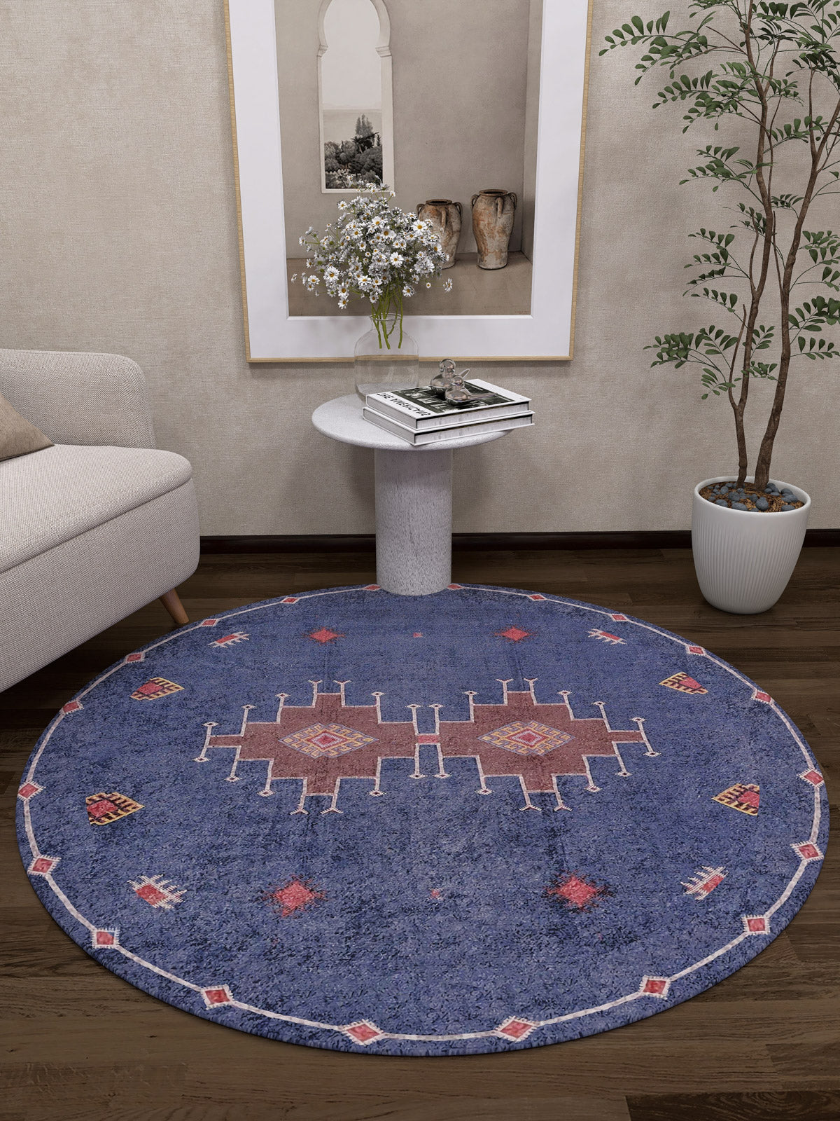 A modern living room with a Wanderer's Way - Washable Rug - JR5101 (Custom Size), a light sofa, white circular side table with flowers, tall potted plant, and decorative accents—perfect for high-traffic spaces.
