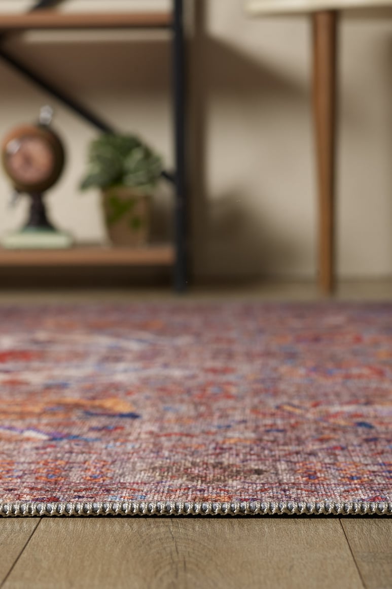 The Velorio Floral Washable Rug - LCC3006 features a vibrant, allergy-friendly design on a wooden floor, with softly blurred shelves and plants in the background—perfect for stylish, easy-care homes.