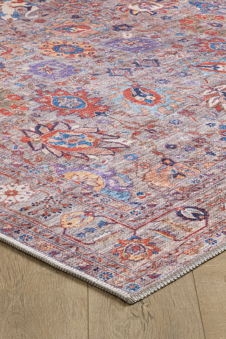 A close-up of the Velorio Floral Washable Rug - LCC3006, allergy-sensitive and ideal for high-traffic areas, featuring purple, red, blue, and orange floral and geometric designs with an intricate border on a light wood floor.