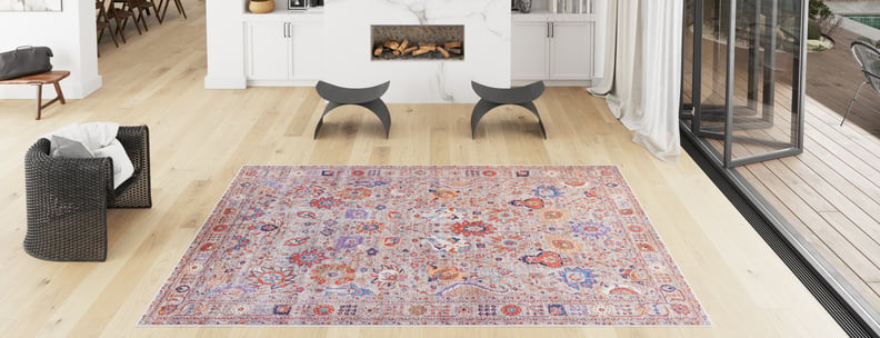 A modern living room with light wood floors, black chairs, a white fireplace, large windows, and the Velorio Floral Washable Rug - LCC3006 (Custom Size) in pink and purple—perfect for allergy-sensitive homes or busy spaces.