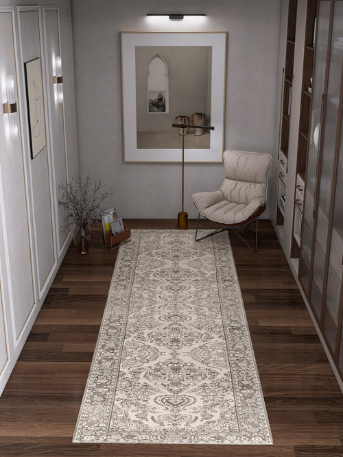 Load image 1 in gallery view. A modern hallway with wooden floors features the Velvet Mosaic - Washable Rug - JRN1004 in a patterned cream design, complemented by an armchair with a cushion, a floor lamp, framed artwork, and bookshelves for stylish convenience.