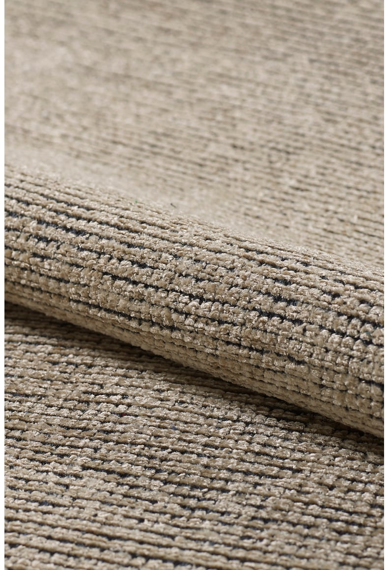 Close-up of the Velvet Touch Beige Area Rug - PST002, featuring a textured beige surface with subtle dark speckles and a soft fold that highlights its contemporary style.