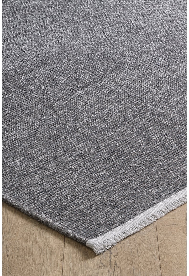 A close-up of the Velvet Touch Dark Gray Area Rug - PST004 with a light fringe edge, displayed on a light wood floor—ideal for those who love modern rugs and minimalist style.