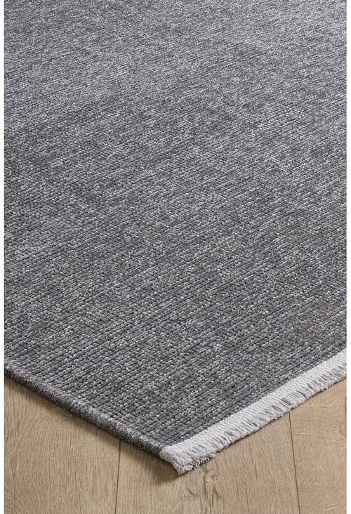Load image 1 in gallery view. A close-up of the Velvet Touch Dark Gray Area Rug - PST004 with a light fringe edge, displayed on a light wood floor—ideal for those who love modern rugs and minimalist style.