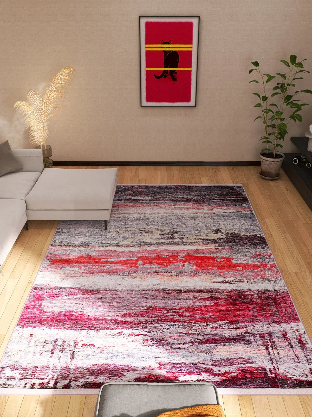 A modern living room with a white sectional sofa, the Vintage Brushed - Washable Rug - JR143 in pink and red, a corner plant, dried pampas grass, and framed cat artwork on the wall.