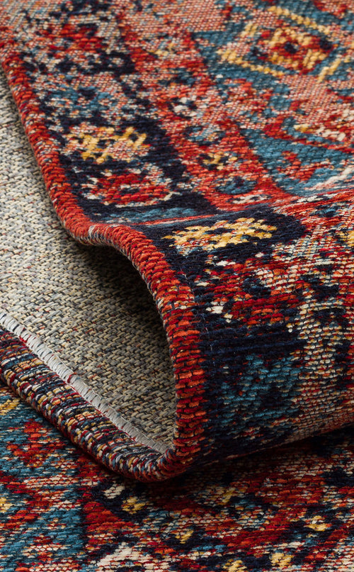 Load image 1 in gallery view. A close-up of the Vintage Echo - Washable Kilims - AND04 shows a rolled-up rug with vibrant red, blue, yellow, and cream hues in intricate geometric and floral patterns bordered by detailed designs.
