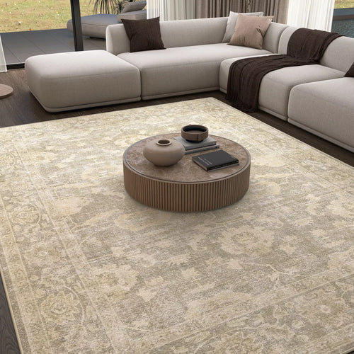 Load image 1 in gallery view. A modern living room with the Vintage Linen - Washable Rug - JRN1028 in light beige—perfect for high-traffic areas—paired with a round wooden coffee table, books, vases, and an L-shaped grey sofa with cozy throws by floor-to-ceiling windows.