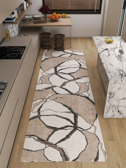 Load image 1 in gallery view. A modern kitchen with light wood floors, a marble island, beige cabinets, and the Vintage Muse - Washable Rug - JRN47 in an abstract branch pattern. A wooden table with fruit and flowers stands near two wooden stools.