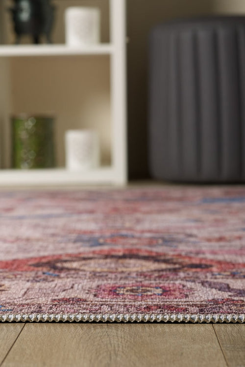Load image 1 in gallery view. Close-up of the edge of the Vivencia Authentic Washable Rug - LCC3016 (Outlet) US on a wooden floor, with a blurred gray ottoman and white shelving unit displaying candles and decor in the background.