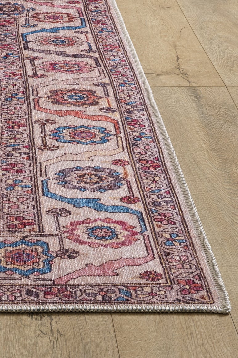 A close-up of the Vivencia Authentic Washable Rug - LCC3016 (Custom Size) with pink, blue, and beige intricate designs on a light wood floor. This allergy-friendly rug features a detailed border and visible edge stitching.