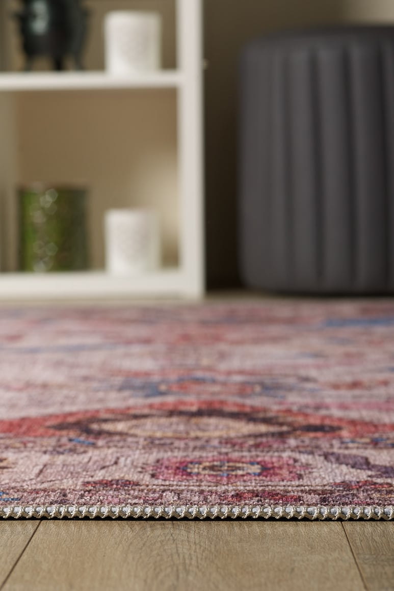 Close-up of the Vivencia Authentic Washable Rug - LCC3016 (Custom Size) with a multicolored pattern on wood flooring; a blurred white shelf and gray pouf in the background—perfect for allergy-sensitive homes.