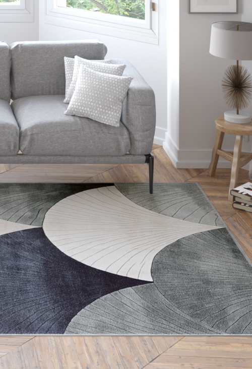 Bild 1 in Galerieansicht laden. A modern living room features a grey sofa, two patterned cushions, and the Vivian Modern Washable Area Rug - MDJ010—perfect for high-traffic areas—on wooden floors near large windows, accented by a side table with a lamp.