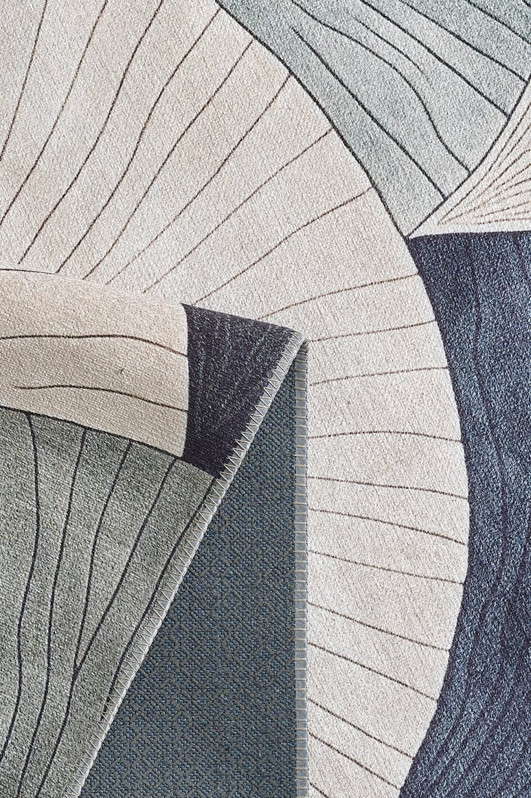 A close-up of the Vivian Modern Washable Area Rug - MDJ010 shows abstract, curved shapes in cream, blue, and gray. One corner is folded to reveal its textured backing—perfect for high-traffic or allergy-sensitive homes.