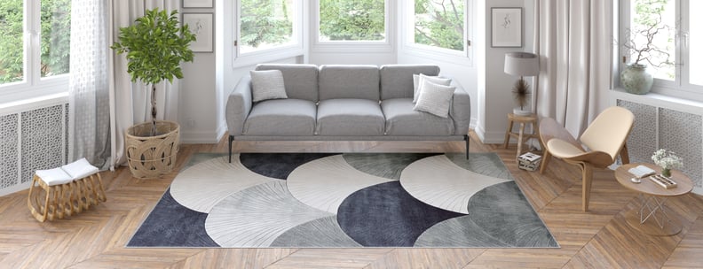 A modern living room with a gray sofa, wooden furniture, potted plant, and large windows with sheer curtains features the Vivian Modern Washable Area Rug - MDJ010—ideal for allergy-sensitive households and high-traffic areas.