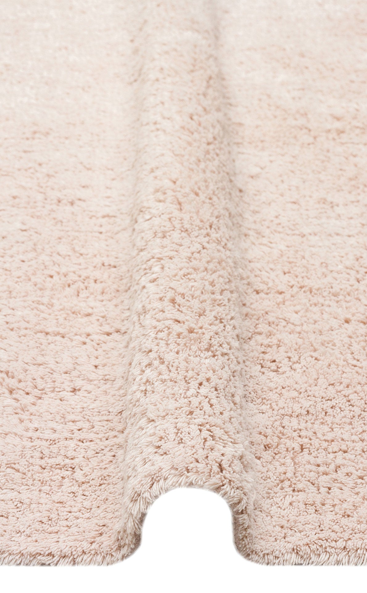A close-up of the Warm Sand - Washable Shaggy - CBNPLAIN rug reveals its cream beige cotton texture, featuring a plush, fluffy surface and a raised, wave-like fold running vertically down the center.