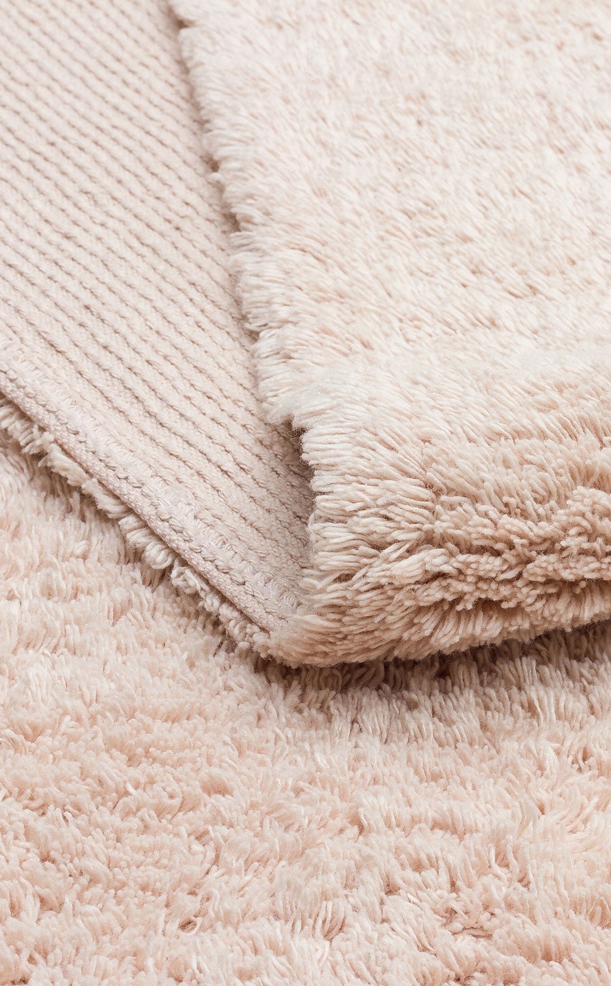 A close-up of the Warm Sand - Washable Shaggy - CBNPLAIN rug shows its plush cream-beige surface and textured underside—ideal as a cozy, washable accent for any space.