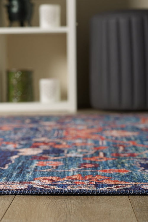Load image 1 in gallery view. A close-up of the Whisper Authentic Blue Washable Rug - LCC3034 on a wooden floor, ideal for high-traffic areas, with a white shelf and gray ottoman softly blurred in the background.