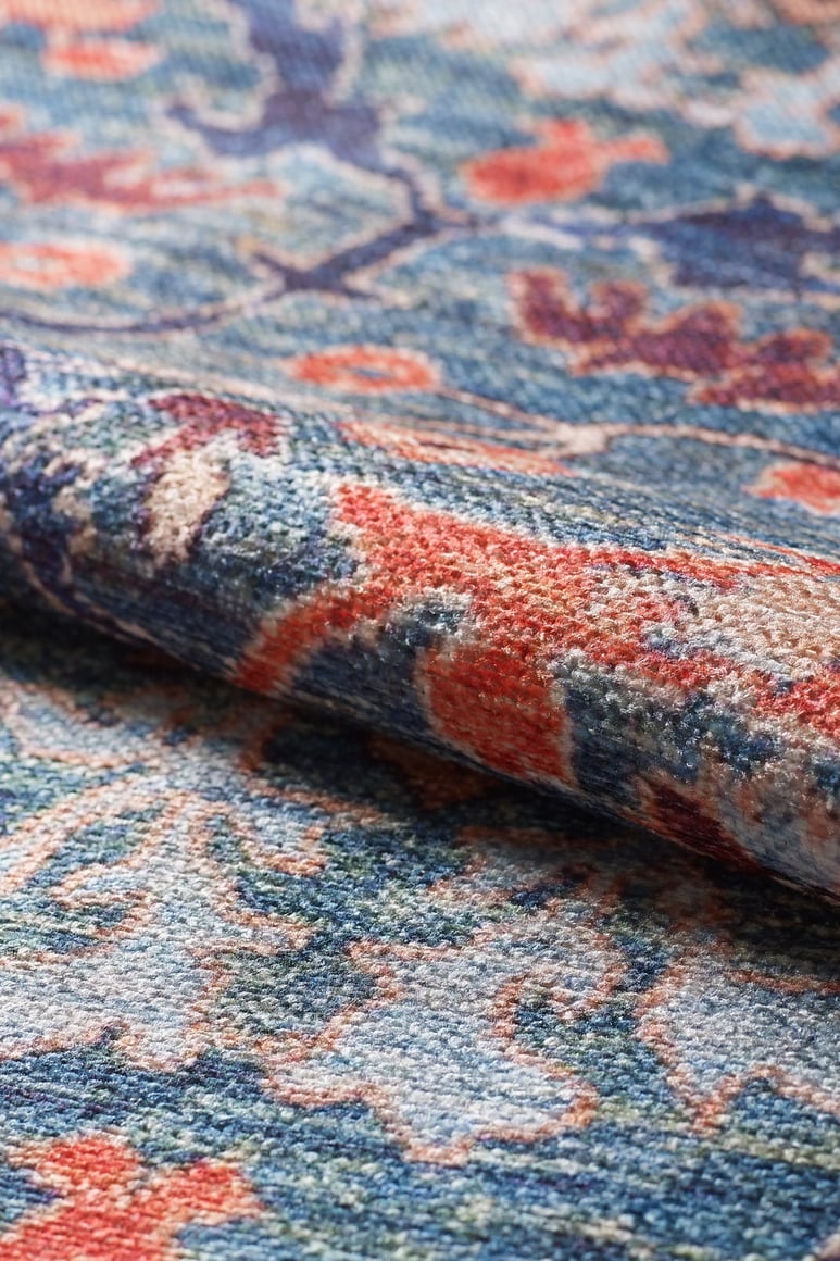 A close-up of the Whisper Authentic Blue Washable Rug - LCC3034 shows its rolled edge and intricate blue, orange, and beige floral and abstract patterns—perfect for high-traffic areas.