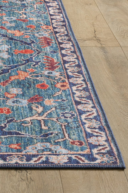 Load image 1 in gallery view. A close-up of the Whisper Authentic Blue Washable Rug - LCC3034 (Custom Size) with a blue border and intricate floral patterns in blue, red, and beige, displayed on a light wood floor—ideal for high-traffic areas.