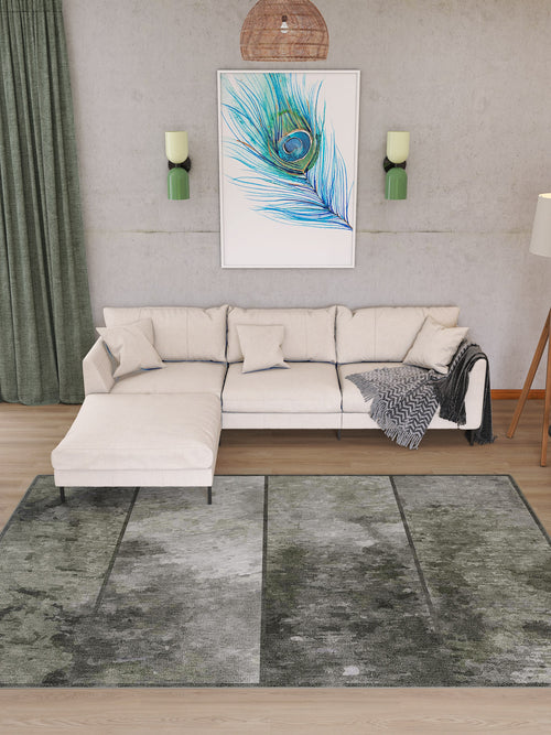 Load image 1 in gallery view. A modern living room features a light sectional sofa, green curtains, a floor lamp, peacock feather wall art, and the Wistful Pattern - Washable Rug - JRN35 in grey-green—ideal for high-traffic areas; light grey walls with sconces frame the art.
