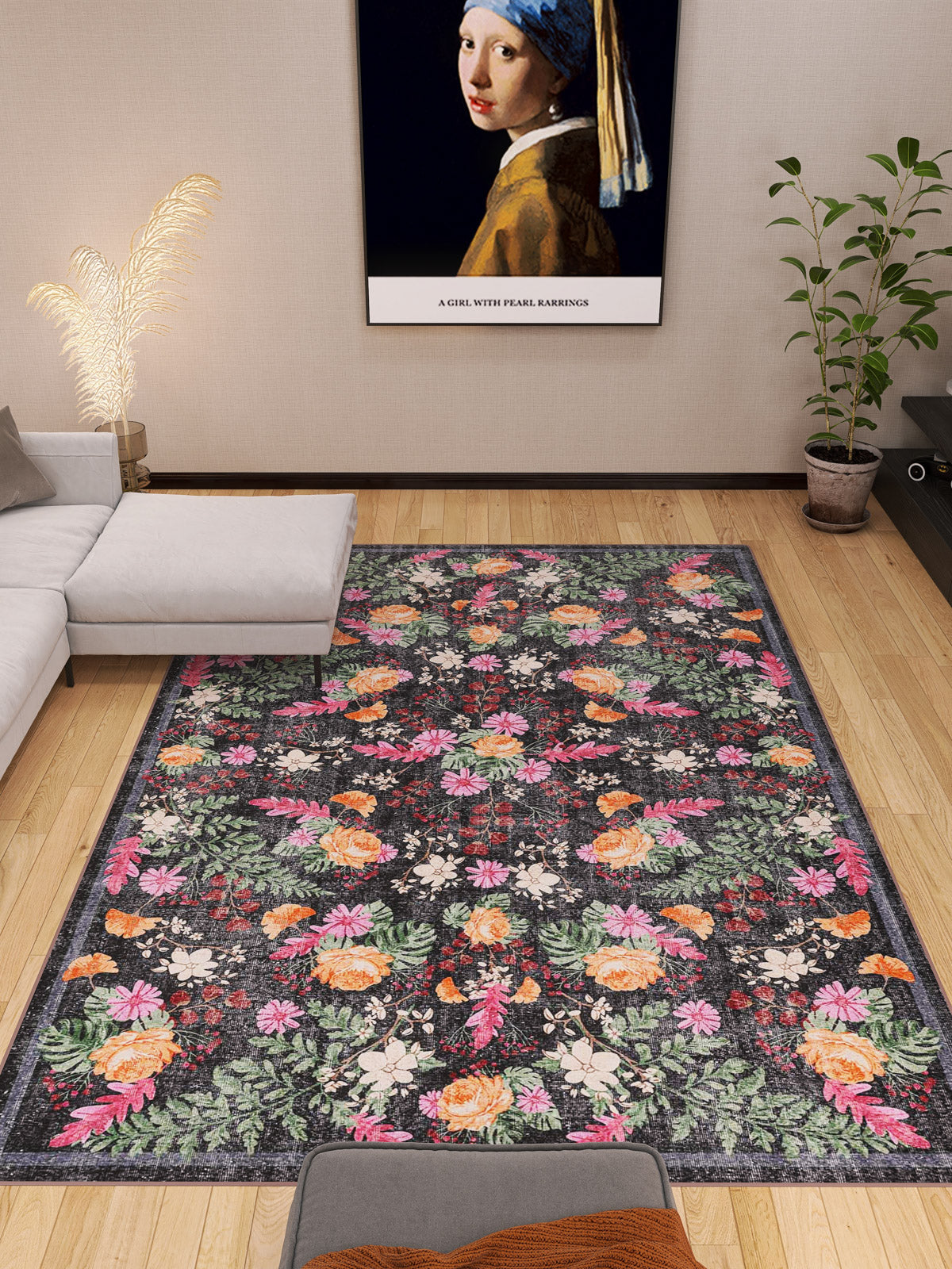 A modern living room with a gray sectional sofa, a large Woven Grace - Washable Rug - JRN28 with floral patterns, a potted plant, and a framed print of Girl with a Pearl Earring on the beige wall above the sofa.