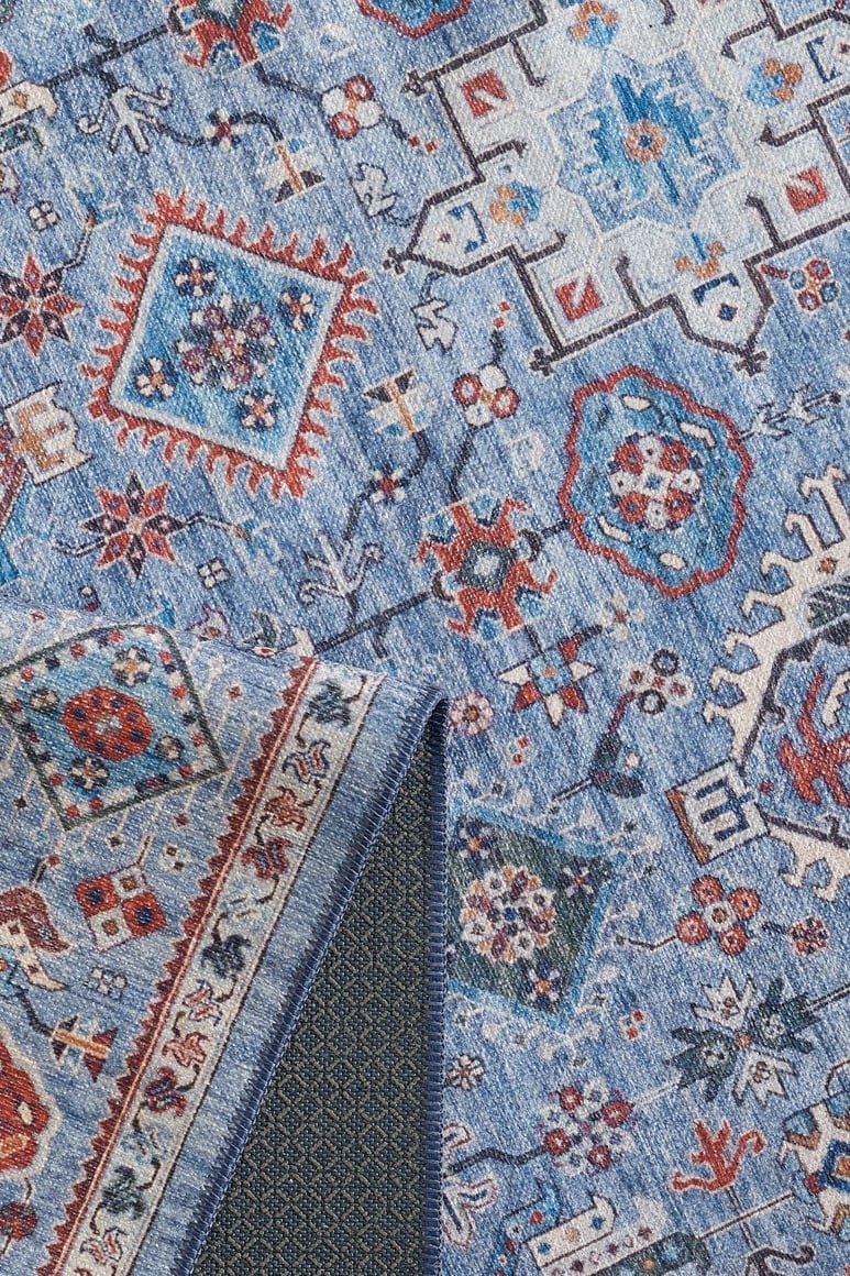 The Xanadu Handmade-Design Blue Washable Rug - LCC3013 (Custom Size) features intricate geometric and floral patterns in red, white, and orange. A folded corner shows its textured dark backing—stylish, practical, and washable.