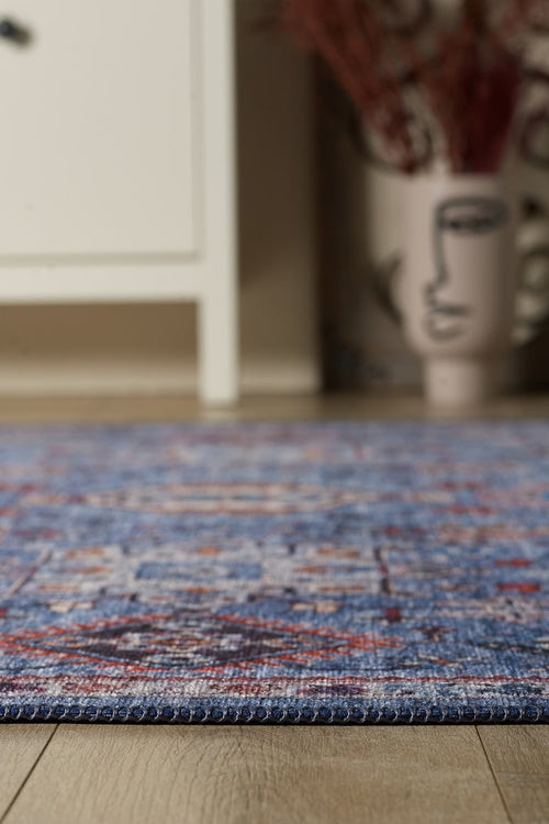 Load image 1 in gallery view. Close-up of the Xanadu Handmade-Design Blue Washable Rug - LCC3013 (Custom Size) with a flat weave on a wooden floor; in the background, a white cabinet and an abstract-face vase with dried branches.