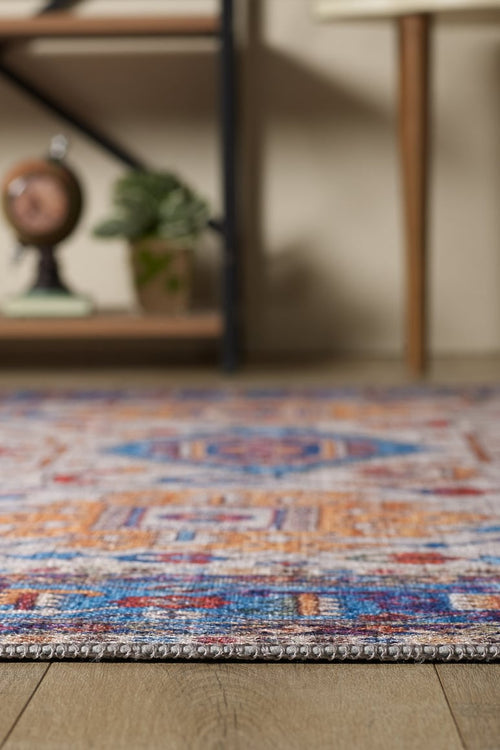 Load image 1 in gallery view. A close-up of the Yonder Blue Cream Washable Rug - LCC3045 on a wooden floor, with blurred shelves, a plant, and a small globe in the background—ideal for adding style to high-traffic spaces.