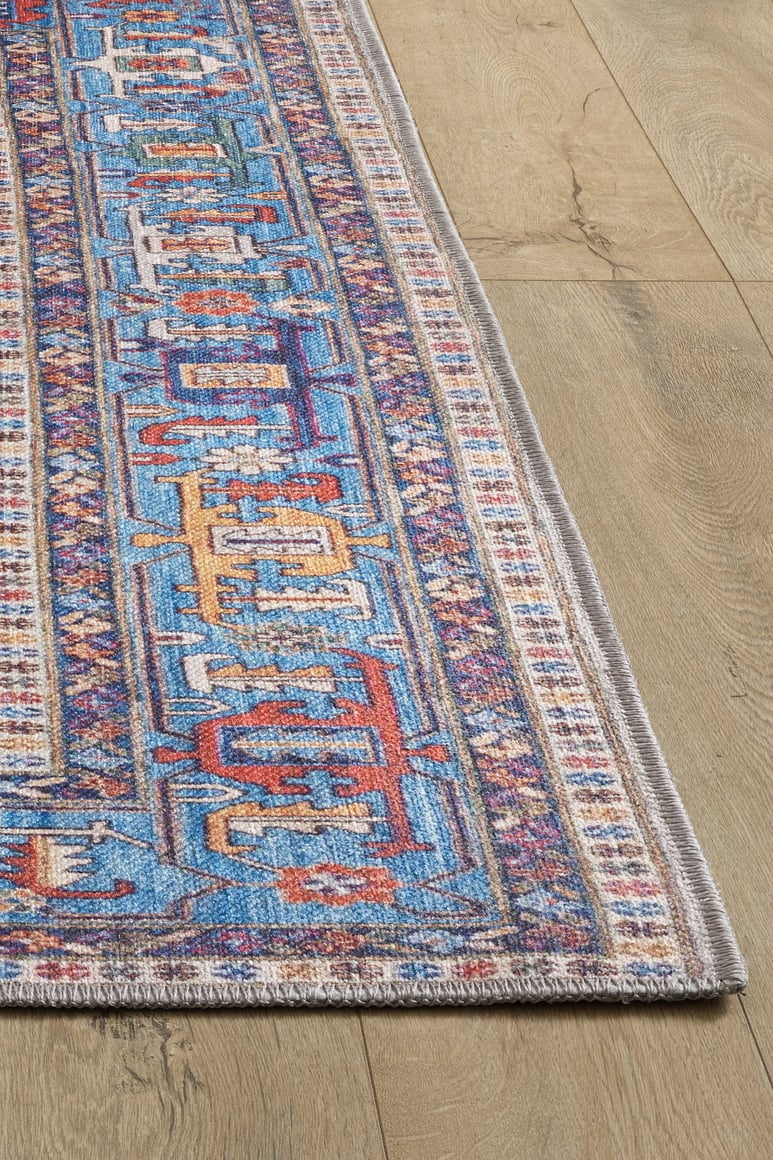 The Yonder Blue Cream Washable Rug (LCC3045) features vibrant multicolor geometric designs with intricate borders and fringed edges. Ideal for high-traffic areas, it sits beautifully on a light wood floor and is easy to clean.