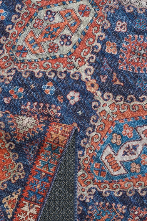 Bild 1 in Galerieansicht laden. Close-up of the Zephyro Kilim-Design Washable Rug - LCC3008, featuring intricate geometric and floral patterns in blue, red, and cream. A folded corner reveals its detailed underside—perfect for high-traffic areas.