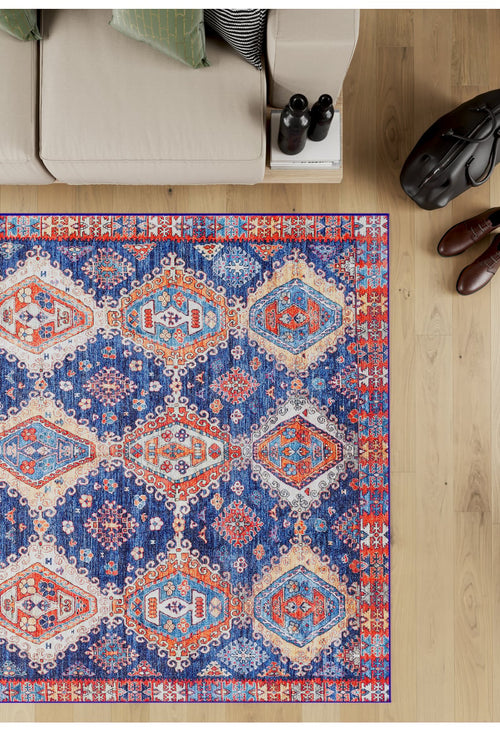 Load image 1 in gallery view. The Zephyro Kilim-Design Washable Rug - LCC3008 (Custom Size) with vibrant geometric patterns lies on a wooden floor by a beige sofa with green cushions—ideal for allergy-sensitive, high-traffic homes. Nearby: black bag, two bottles, brown shoes.